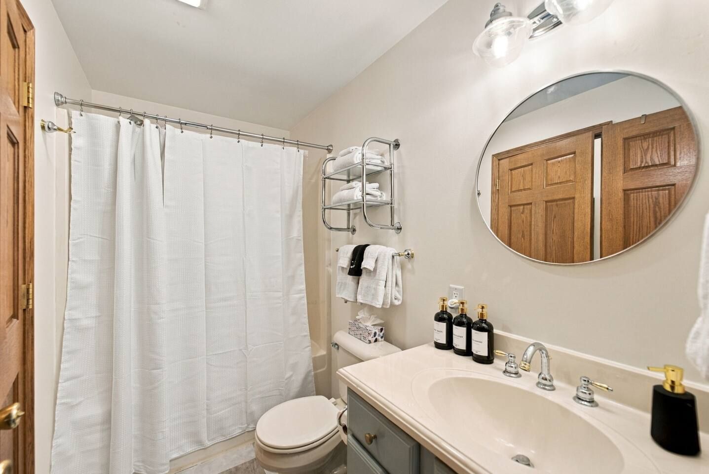 Bright full bath with modern vanity, round mirror, and stocked essentials