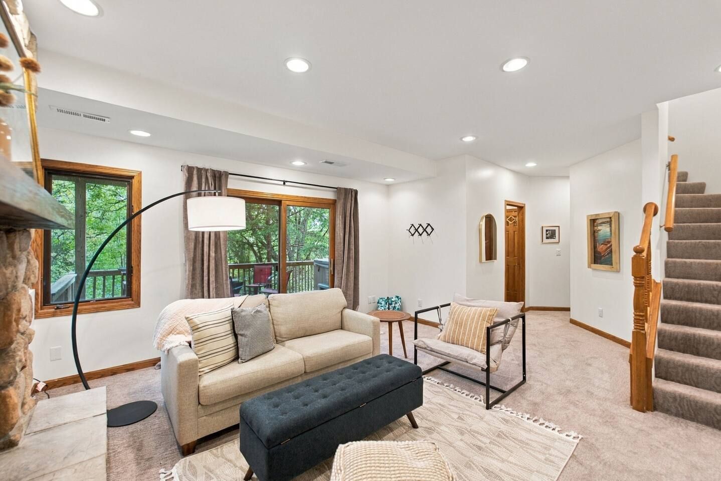 A spacious living room with a sofa, a chair, a bench, a staircase, and a view of the outdoors.
