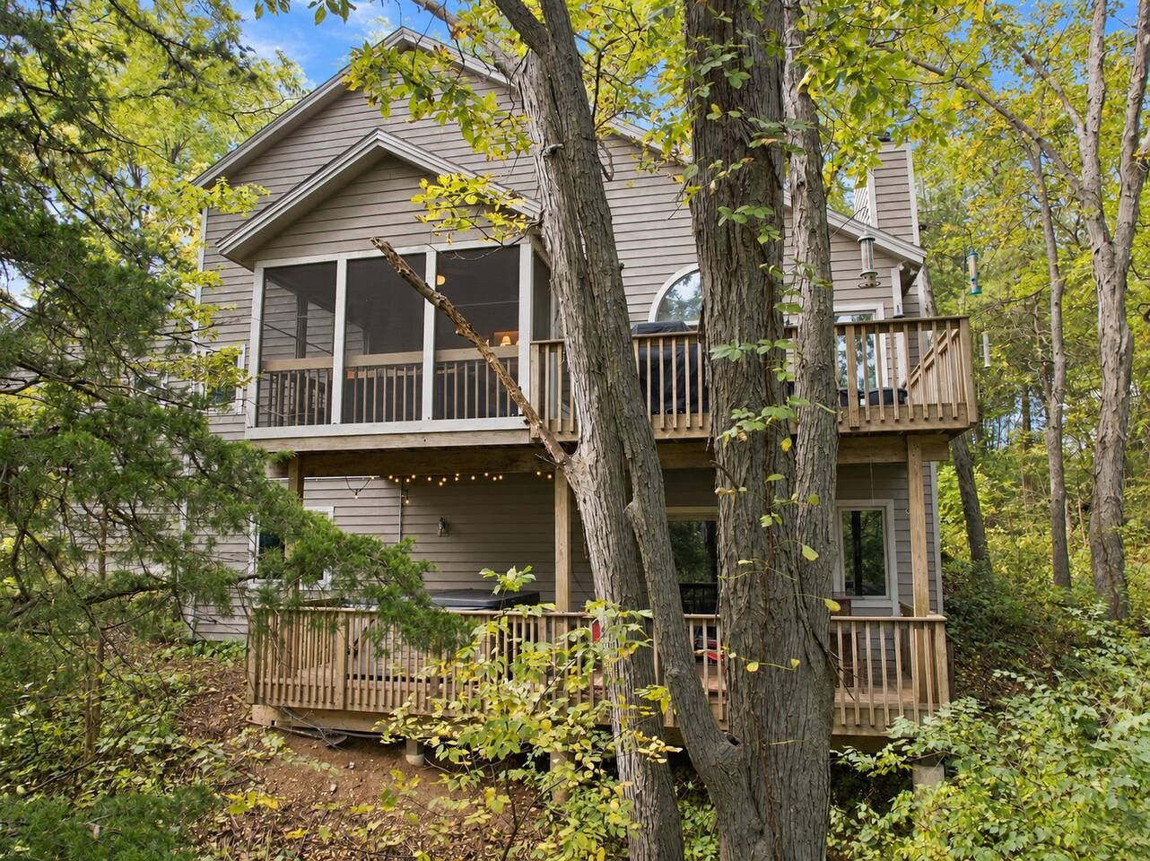 A two-story house with a balcony and a deck, surrounded by trees.