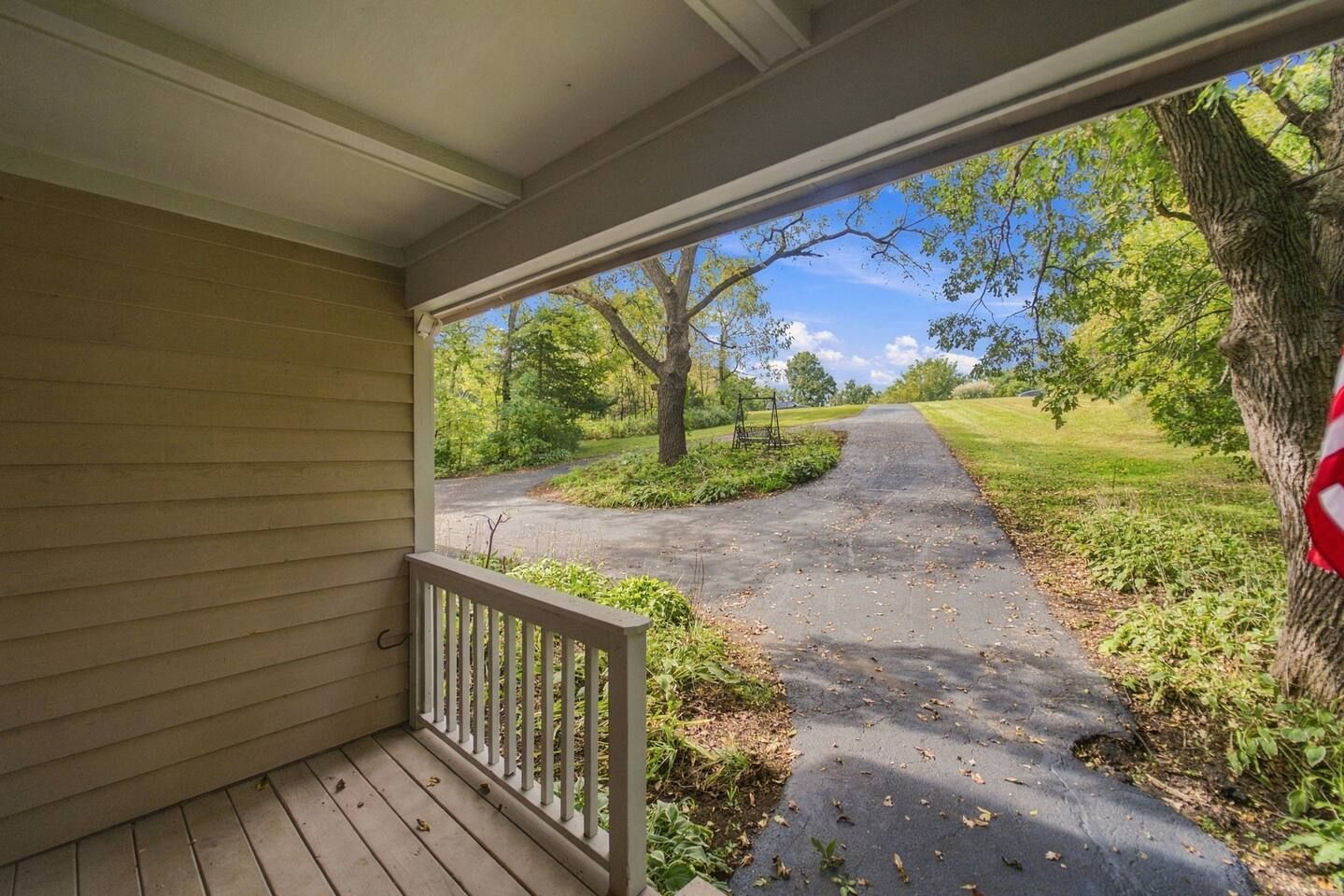 A porch with a view of a paved path leading to a grassy area with trees.
