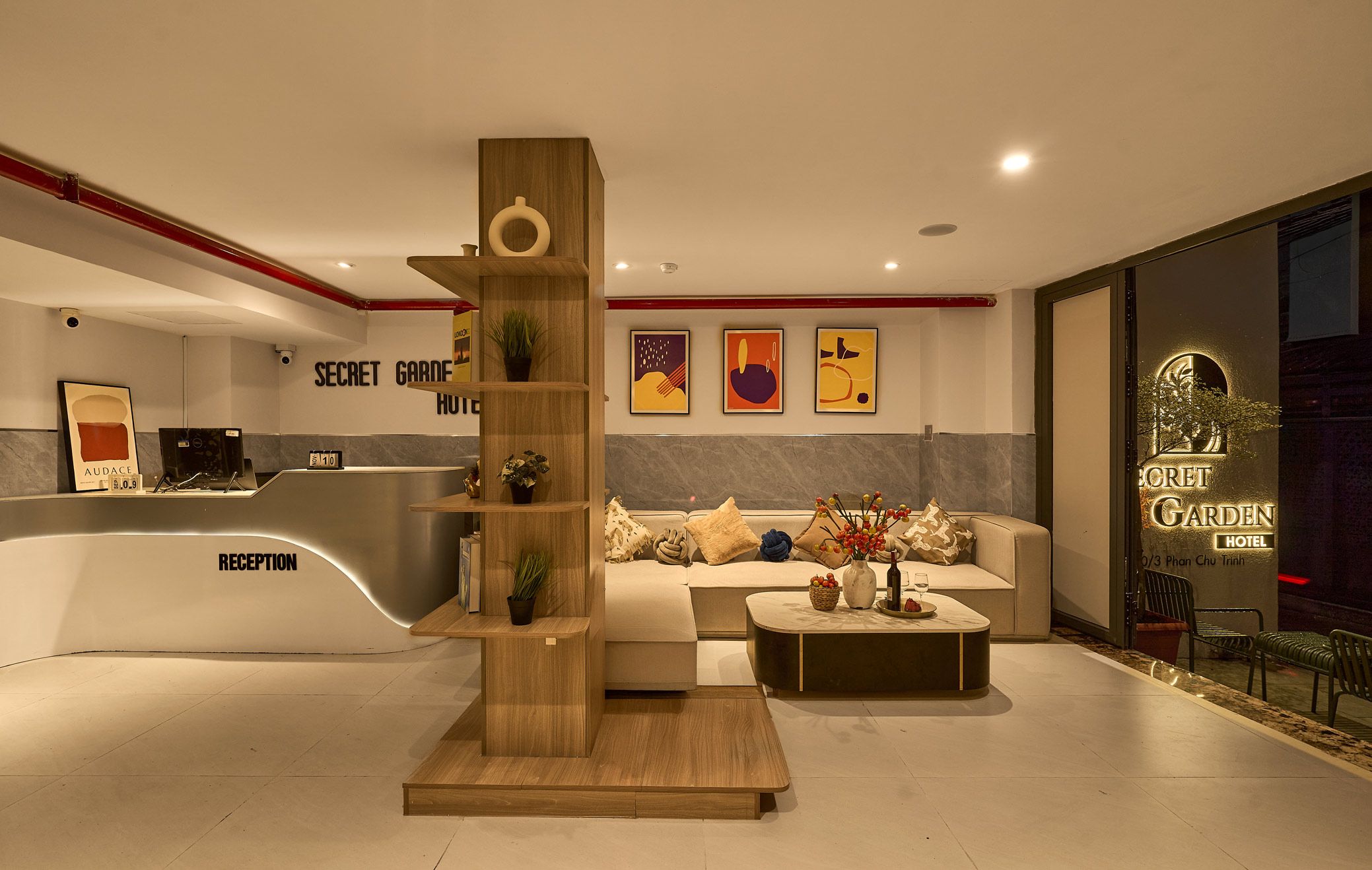 Ein Hotel-Empfangsbereich mit modernem Design, inklusive einer Rezeption, einer Couch mit Zierkissen und einem Holz-Pflanzenständer.