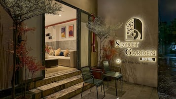 L’extérieur de l’hôtel Secret Garden, avec une enseigne, des marches menant à l’entrée et des sièges installés à l’extérieur.