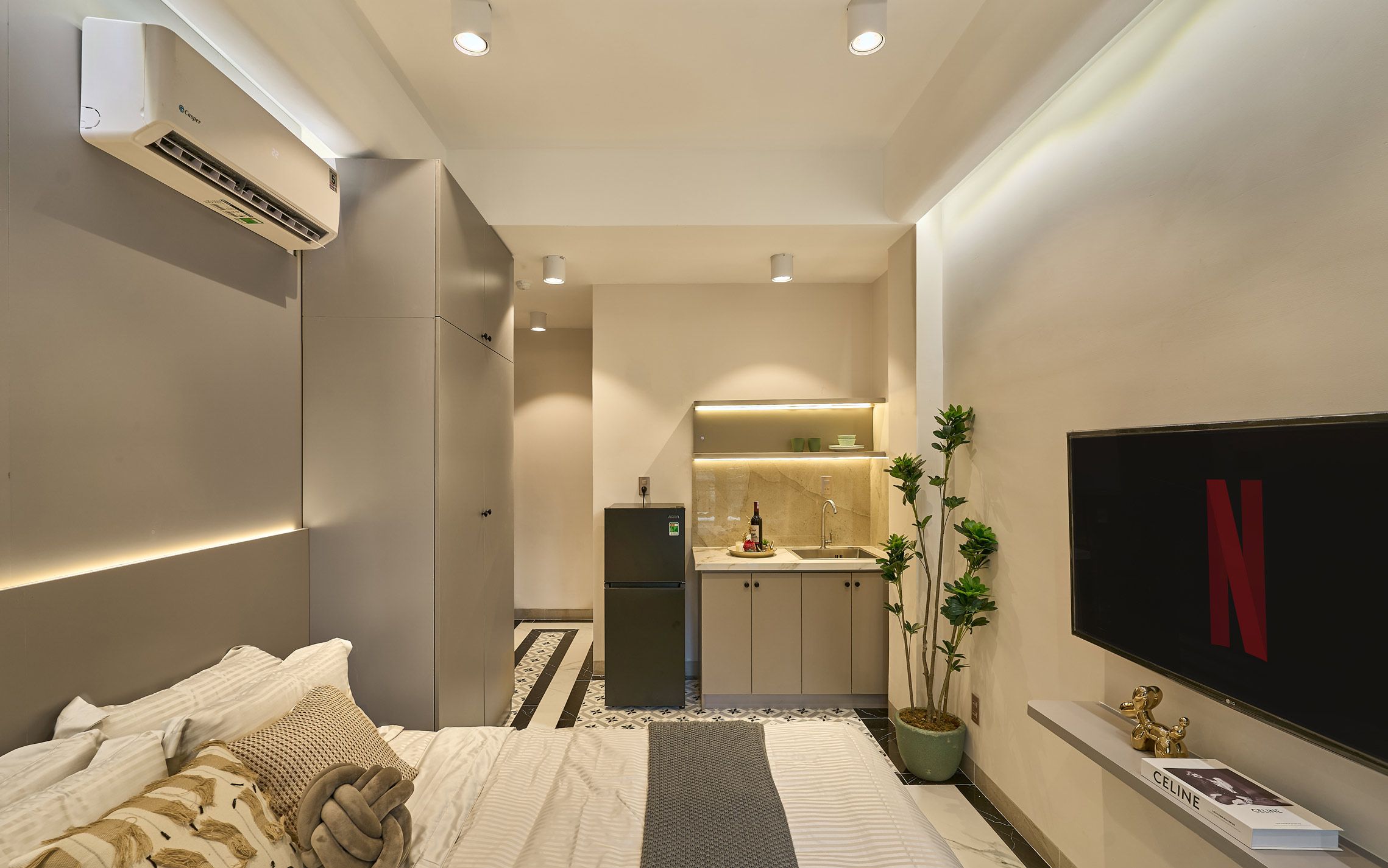 Une chambre d’hôtel de taille réduite, comprenant un lit, une petite kitchenette, un téléviseur et une plante en pot.