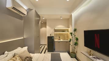 Une chambre d’hôtel de taille réduite, comprenant un lit, une petite kitchenette, un téléviseur et une plante en pot.