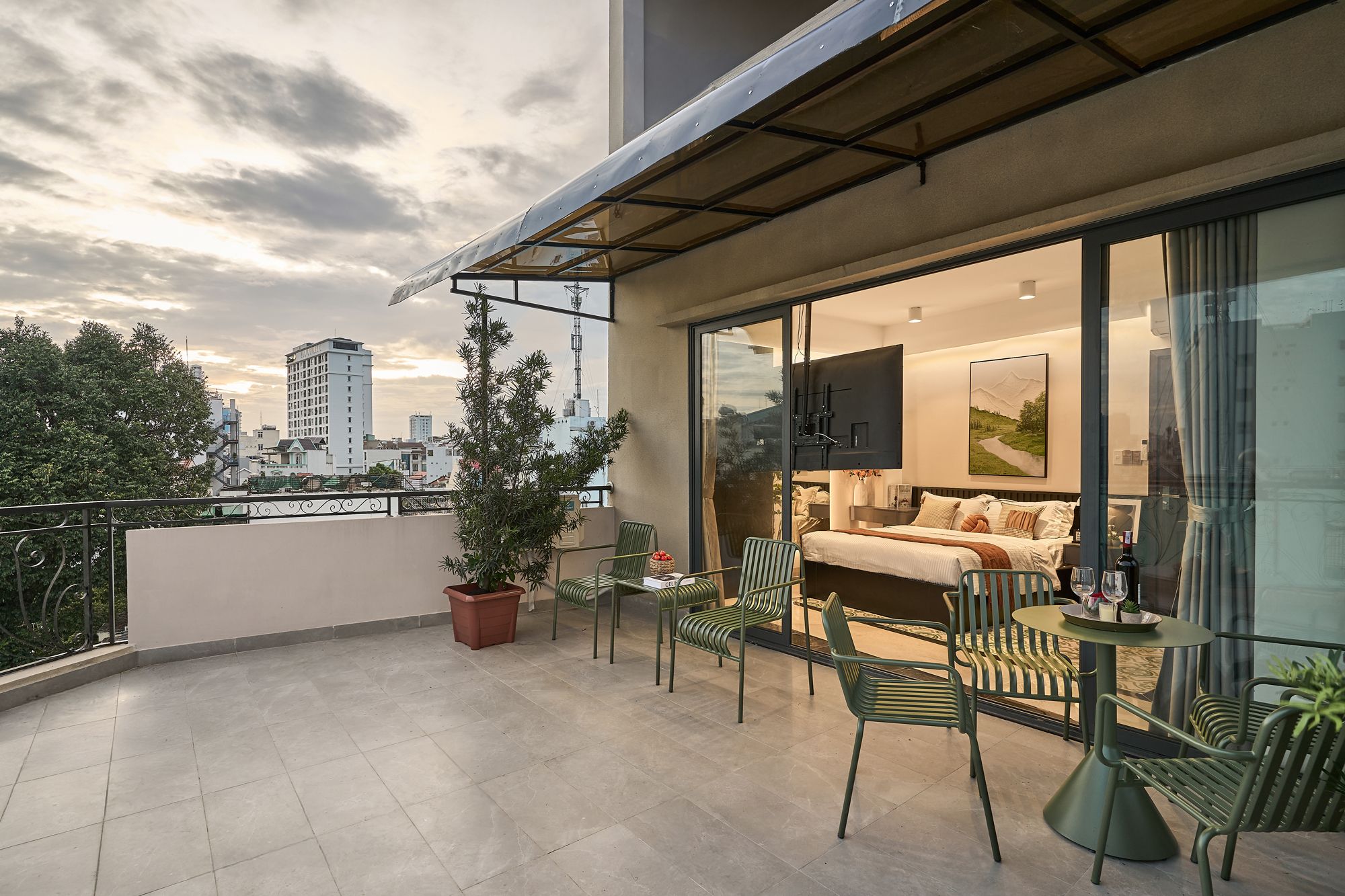 Un balcon aménagé avec un canapé, des chaises et une table, d’où l’on peut admirer une vue sur la ville, avec ses bâtiments et un arbre.