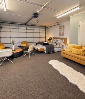 Une chambre à coucher moderne avec un lit, deux chaises, un canapé, une petite table et un tapis blanc et moelleux.