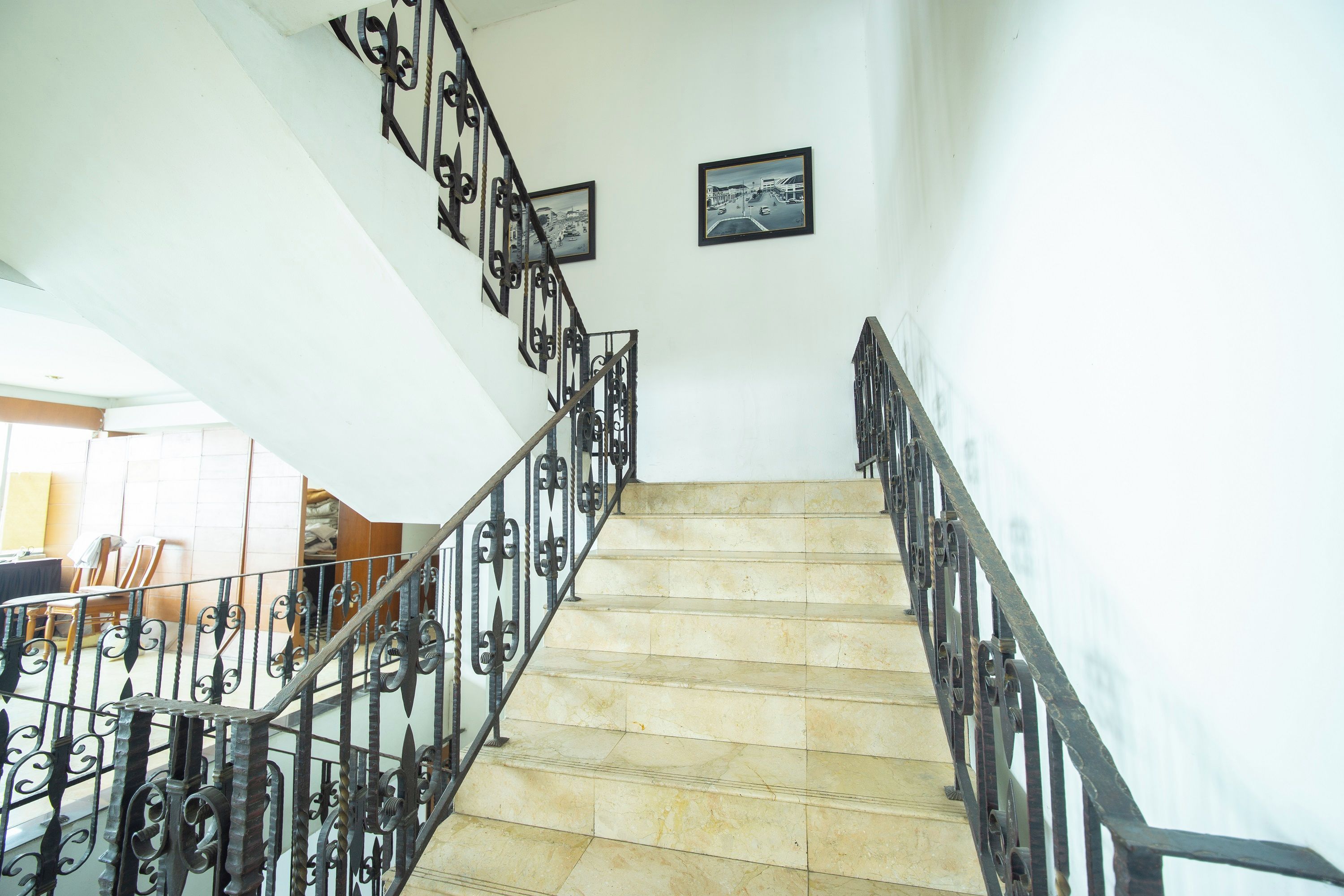 Una escalera con barandillas metálicas ornamentales y piso de baldosas, que conduce a un nivel superior.