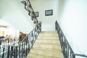 Una escalera con barandillas metálicas ornamentales y piso de baldosas, que conduce a un nivel superior.