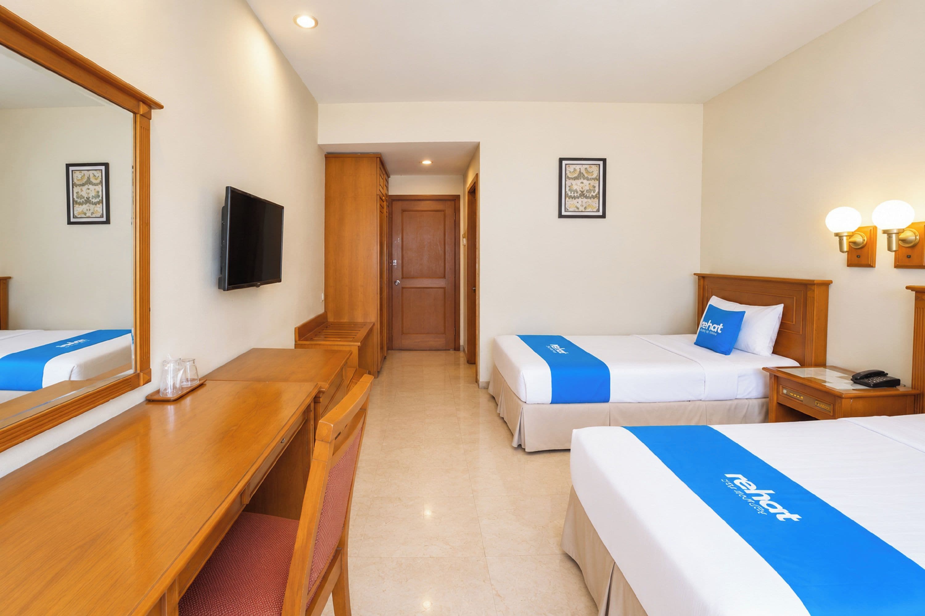 A hotel room with two beds, a desk, a mirror, a television, and a door leading to another room.