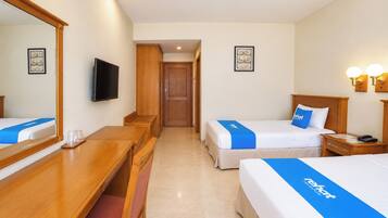 A hotel room with two beds, a desk, a mirror, a television, and a door leading to another room.