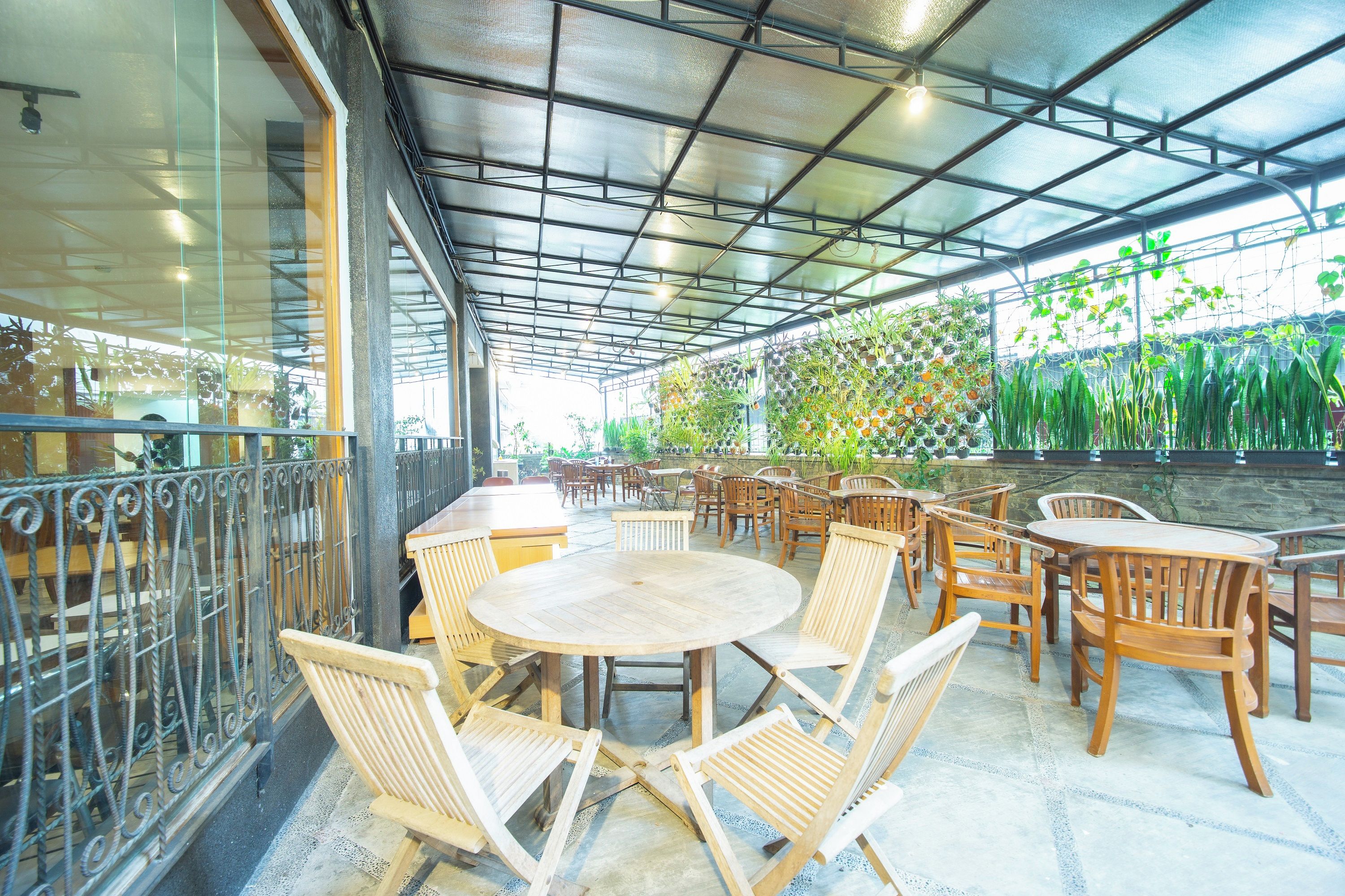 An outdoor cafe area with round tables and wooden chairs, surrounded by a glass railing.