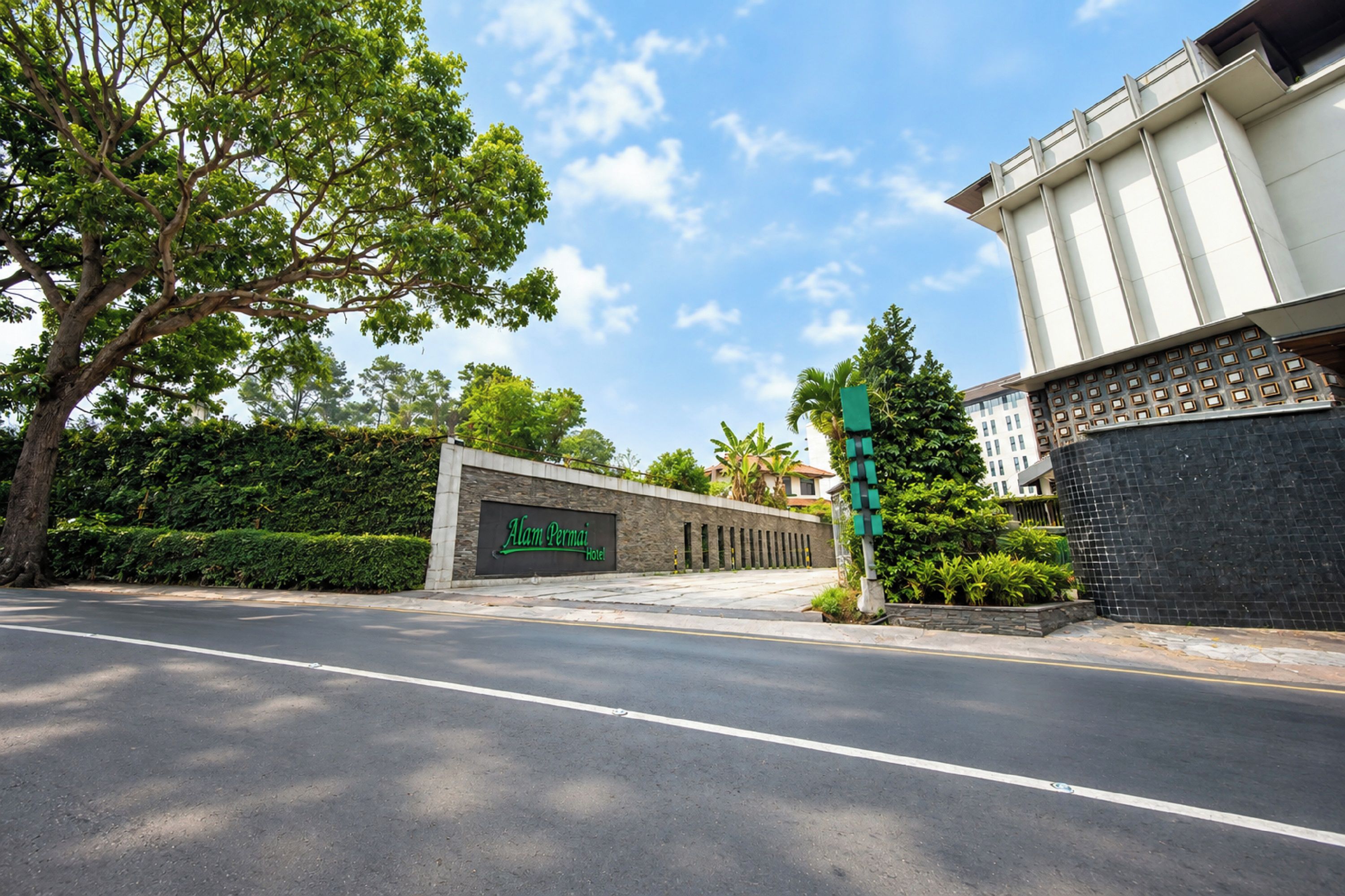 A hotel entrance with a sign, a road, and a building with a modern design.
