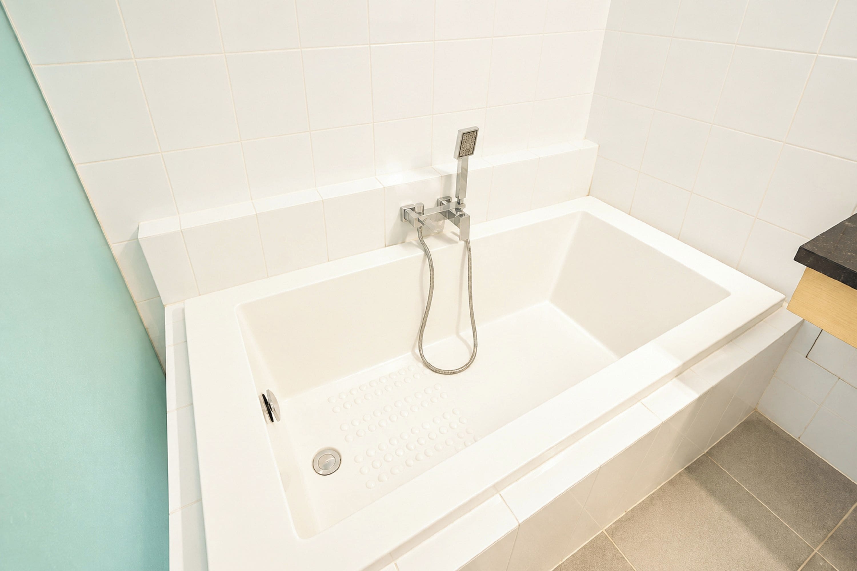 A modern bathroom with a white bathtub, a handheld showerhead, and a visible drain.