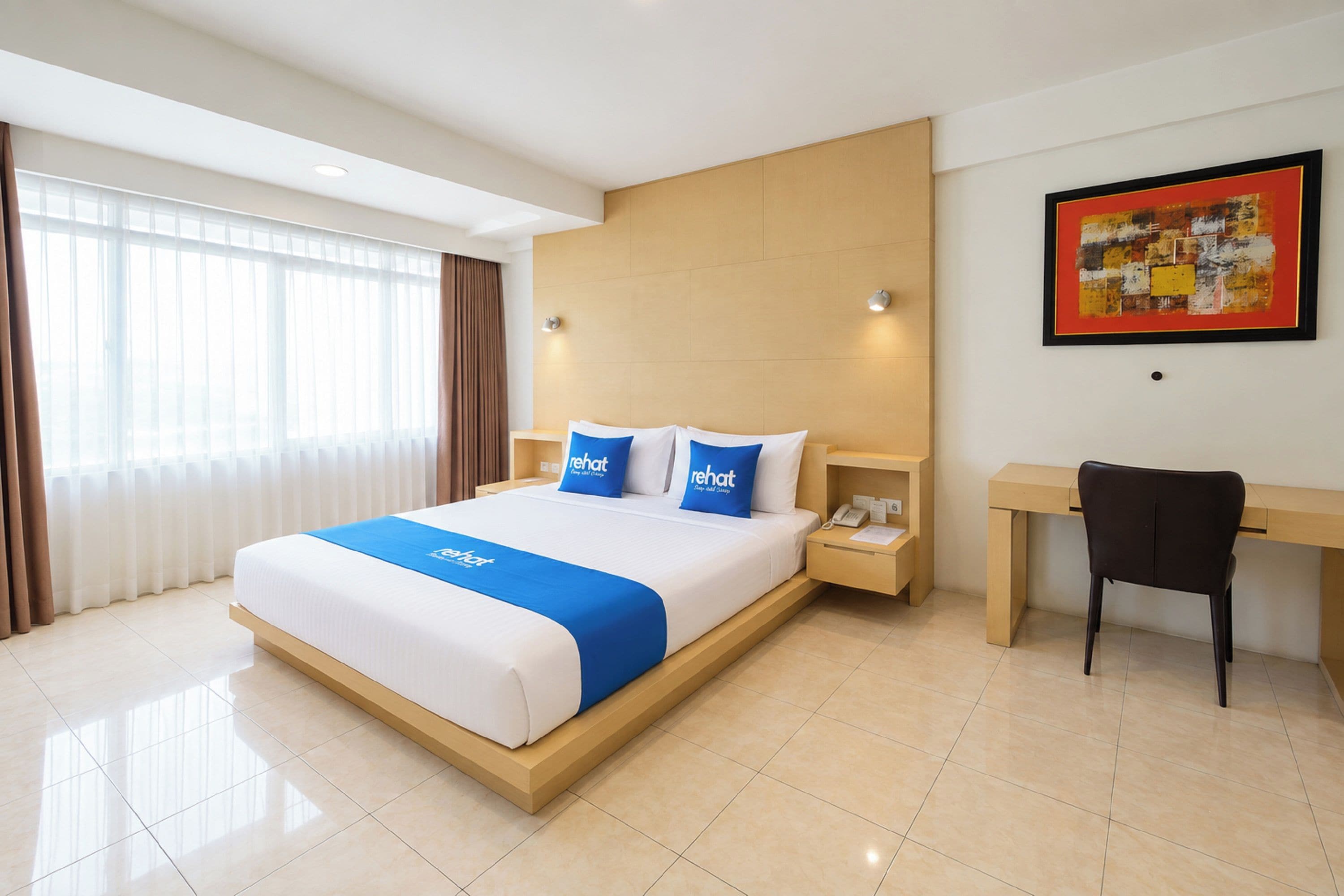 A hotel room with a bed, a desk, a chair, and a painting on the wall.