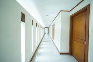 Un pasillo largo y estrecho con paredes blancas y puertas de madera, que conduce a una habitación luminosa al final.