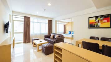 Una habitación de hotel con sofá, reposapiés, mesa de centro y un área de comedor con sillas y mesa.