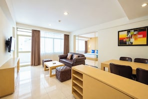Una habitación de hotel con sofá, reposapiés, mesa de centro y un área de comedor con sillas y mesa.