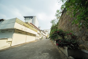A narrow street flanked by buildings with a mix of modern and traditional architecture, a clear sky, and a wall with climbing plants. - Rehat at Hotel Alam Permai (Bandung)