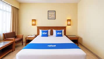 Habitación de hotel con una cama grande, dos mesitas de noche, una silla, un escritorio y una ventana con cortinas.