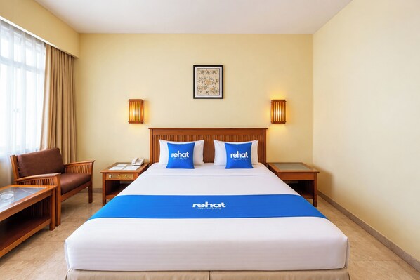 Habitación de hotel con una cama grande, dos mesitas de noche, una silla, un escritorio y una ventana con cortinas.