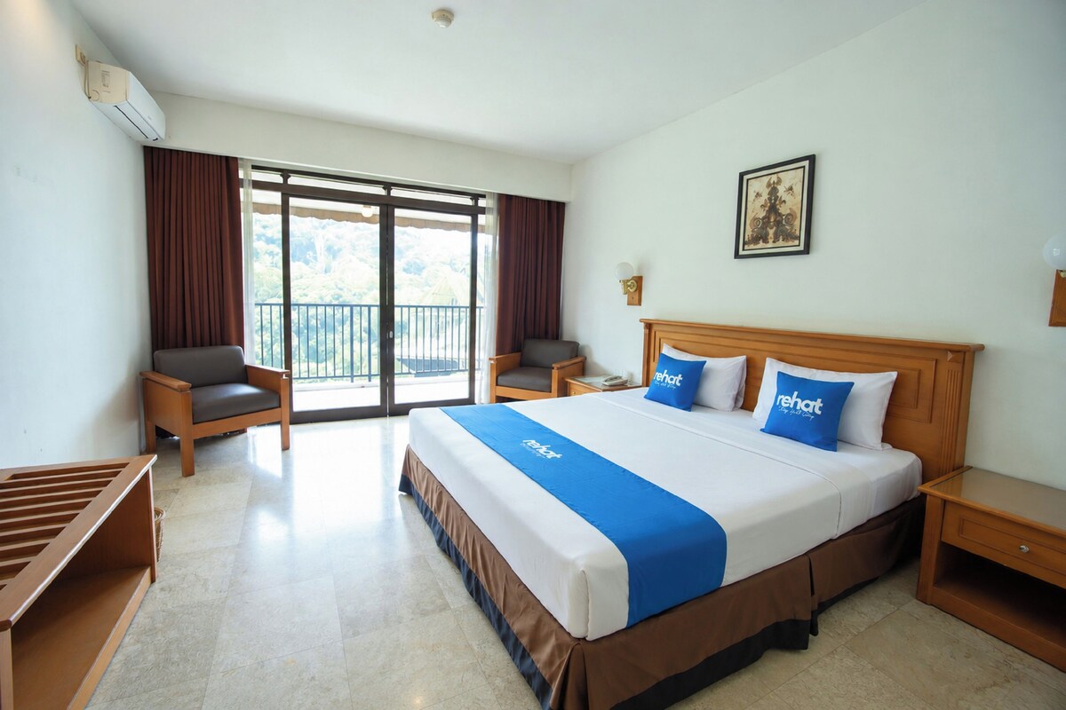 A hotel room with a large bed, two bedside tables, a chair, a balcony, and a window with curtains.