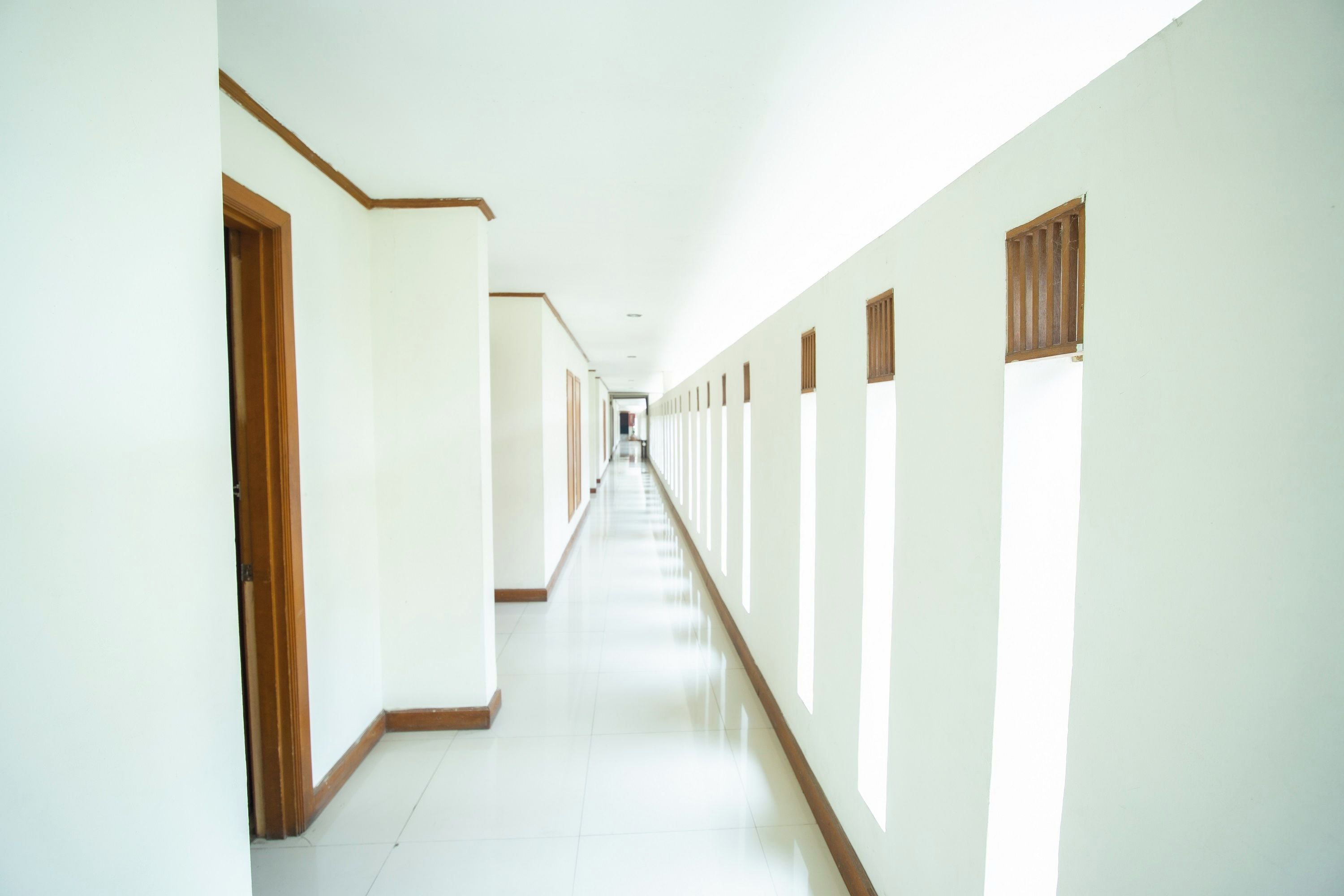 Un long couloir étroit, avec des portes de part et d’autre et des fenêtres sur le côté droit.