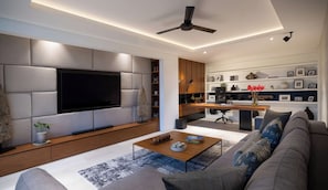 Uma sala de estar moderna com TV de tela plana, um sofá, uma mesa de centro e uma área de cozinha com mesa e cadeiras.