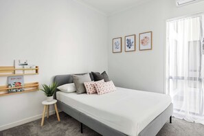 Quarto moderno com cama, mesinha de cabeceira, planta em vaso e estante de livros.