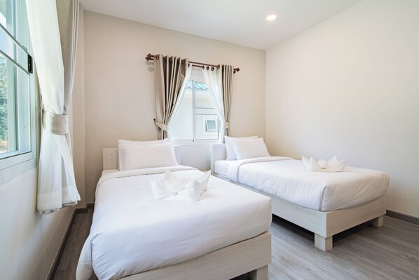 A hotel room with two single beds, a window with curtains, and a wooden floor.