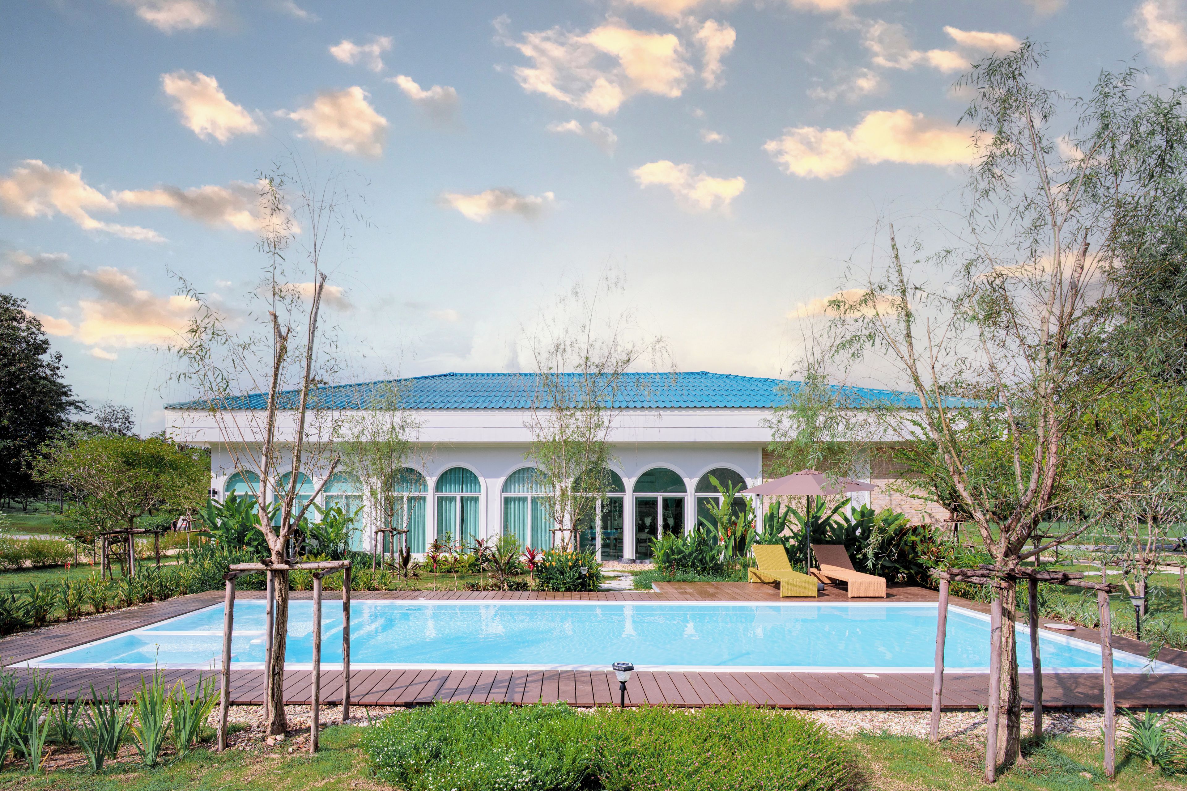 A pool area with a clear sky, a building with arched windows, and a blue roof.
