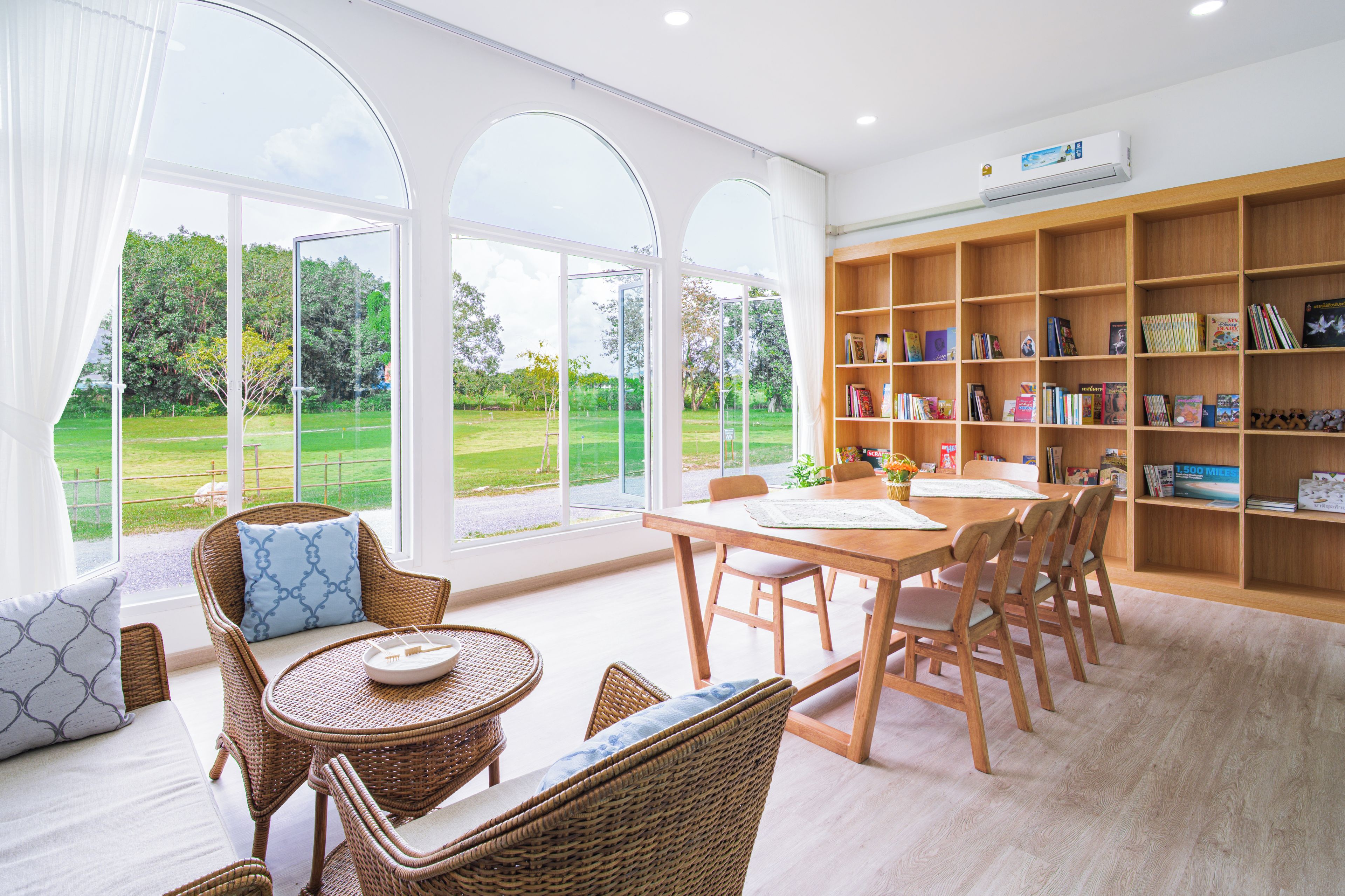 A spacious room with a large window, a wooden bookshelf, and a dining area.
