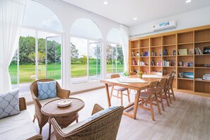 A spacious room with a large window, a wooden bookshelf, and a dining area.