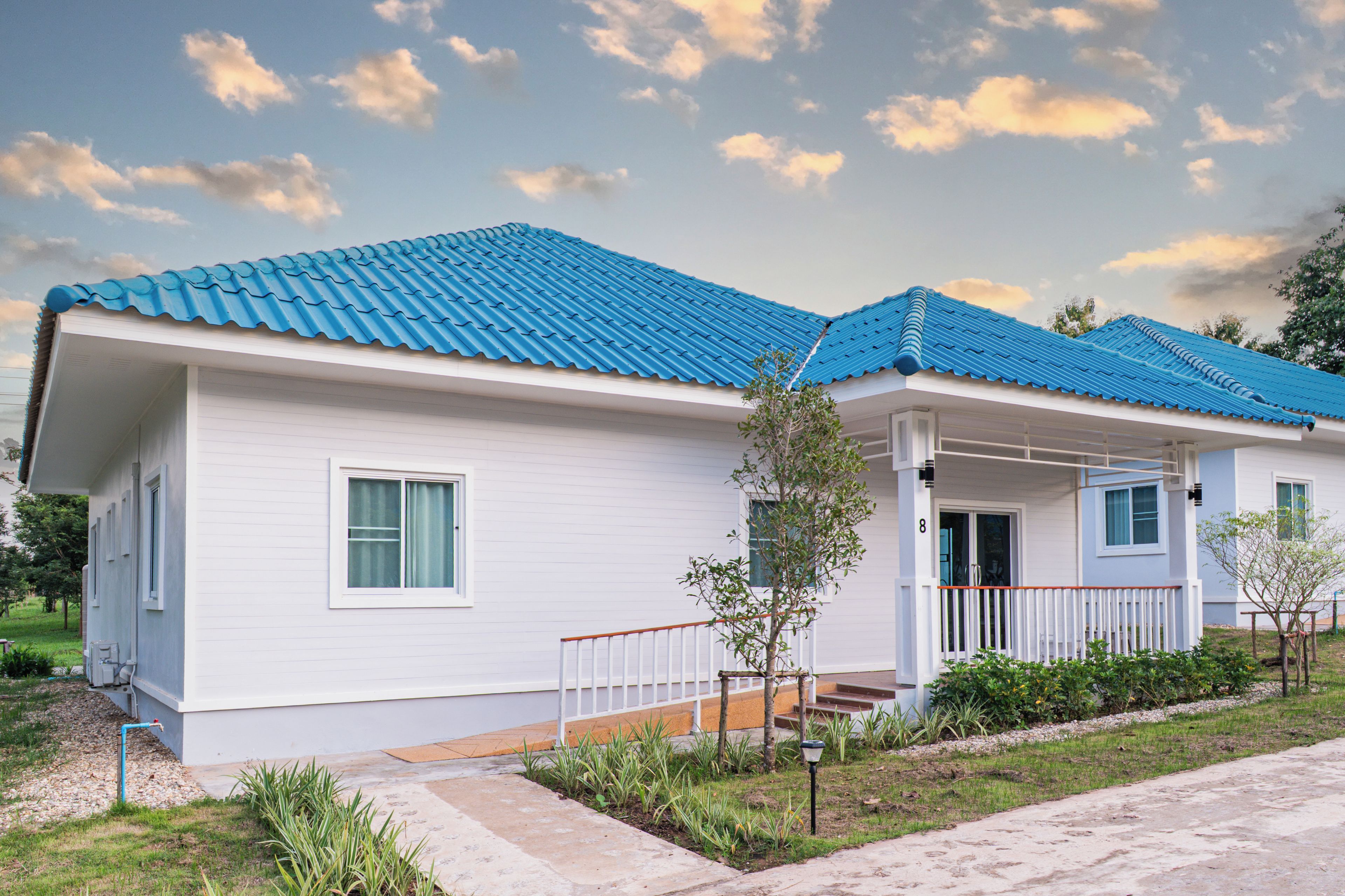 A single-story house with a blue tiled roof, white siding, and a front porch with a railing.