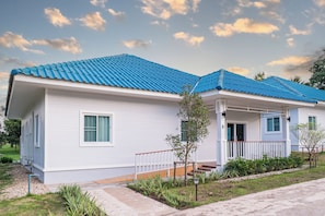 A single-story house with a blue tiled roof, white siding, and a front porch with a railing. - Baan Nam Nan (Phu Phiang)