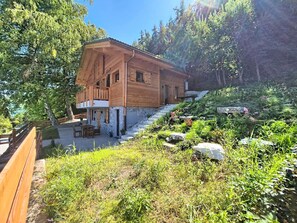 A wooden cabin with a balcony, surrounded by a garden with various plants and rocks. - Byzance 6 by Interhome (Nendaz)