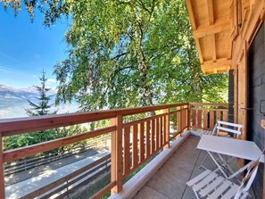 A balcony with a wooden railing, a table with a chair, and a view of a mountain range. - Byzance 6 by Interhome (Nendaz)