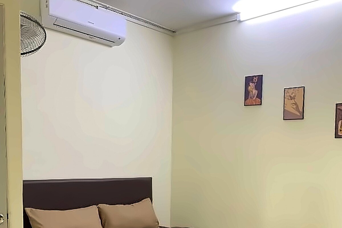 A bedroom with a bed, a wall-mounted air conditioner, and three framed pictures on the wall.