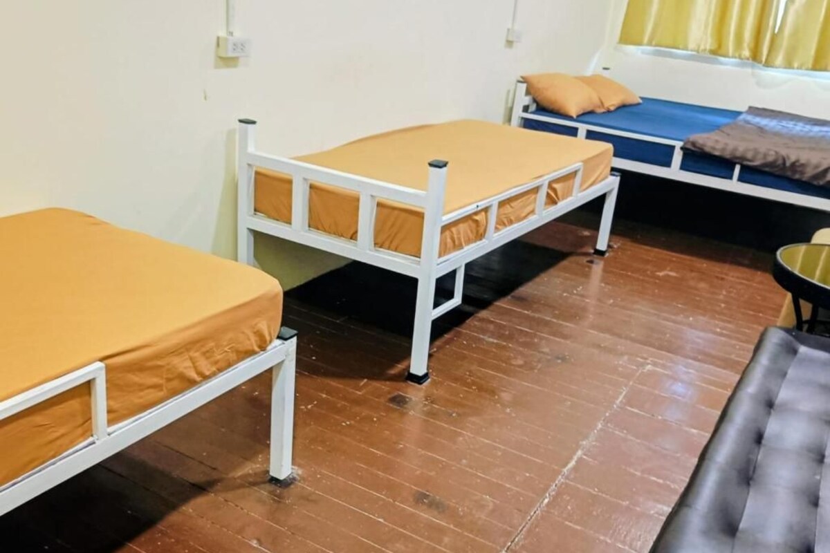 Quarto com duas camas individuais, um banco preto e uma janela com cortinas.