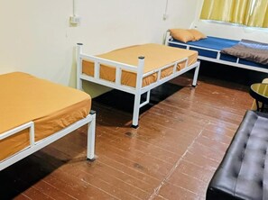 Quarto com duas camas individuais, um banco preto e uma janela com cortinas.