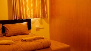A neatly made bed with pillows and a blanket, a bedside table with a lamp, and a wall socket. - The House Hostel 2  (Bangkok)