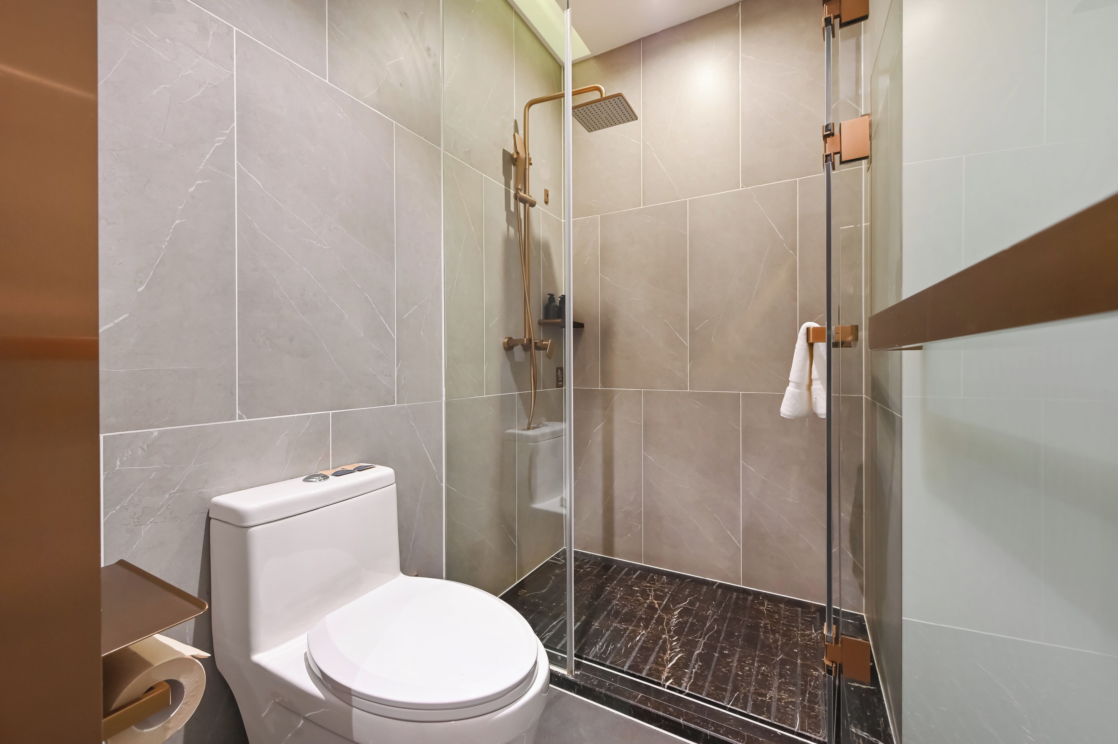 Un baño moderno con inodoro, ducha con puerta de vidrio y suelo de mármol.