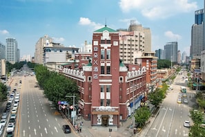 Ein mehrstöckiges Hotel mit einer markanten roten Fassade, an einer belebten Kreuzung in einer Stadt, umgeben von Hochhäusern.