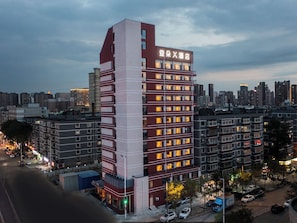 Un hotel de varios pisos con una fachada destacada en rojo y blanco, múltiples balcones y un horizonte urbano al fondo.