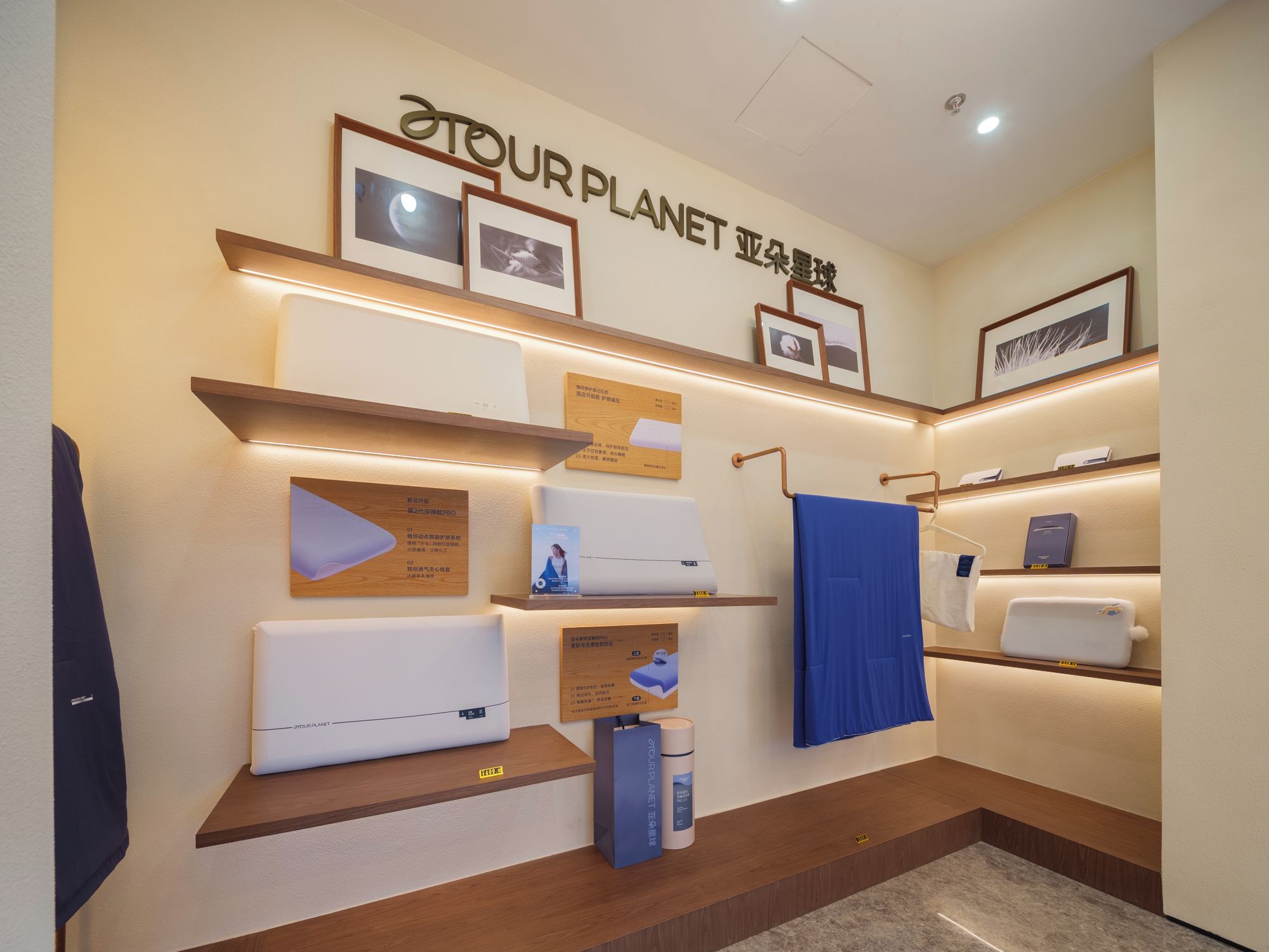 A hotel room with a wall-mounted shelf displaying various items, including a blue towel, a white pillow, and framed pictures.