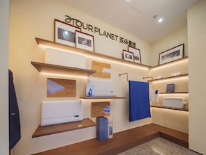 Habitación de hotel con estante fijado a la pared que exhibe diversos objetos, incluyendo una toalla azul, un almohadón blanco y cuadros enmarcados.
