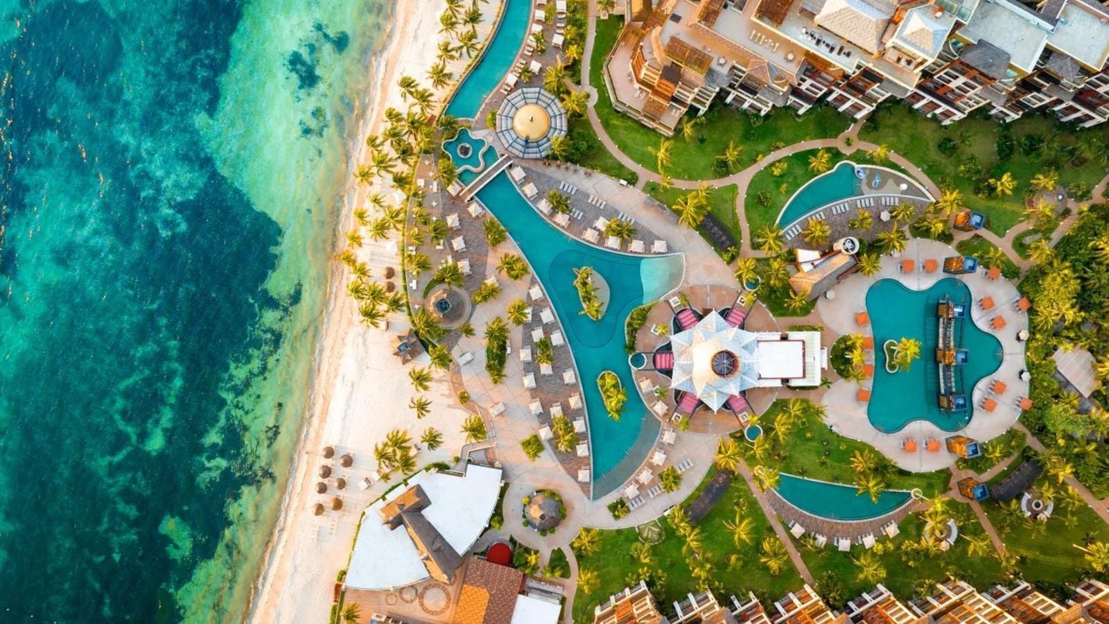 Vista aérea de um resort com várias piscinas, palmeiras e acesso à praia.