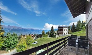 A balcony with a view of a mountain range, a building with multiple balconies, and a grassy area with trees. - Domino C D-1 by Interhome (Nendaz)