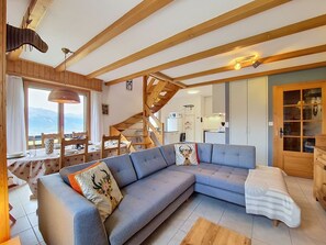 A modern living room with a sectional sofa, wooden beams, a dining area, and a view of the mountains. - Domino C D-1 by Interhome (Nendaz)