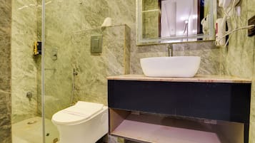 A bathroom with a white toilet, a glass-enclosed shower, a marble wall, a sink with a vessel basin, and a mirror with a towel rack.