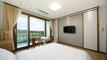 Une chambre d’hôtel avec un lit, un téléviseur fixé au mur, un balcon avec une table et des chaises, et une grande fenêtre avec des rideaux.